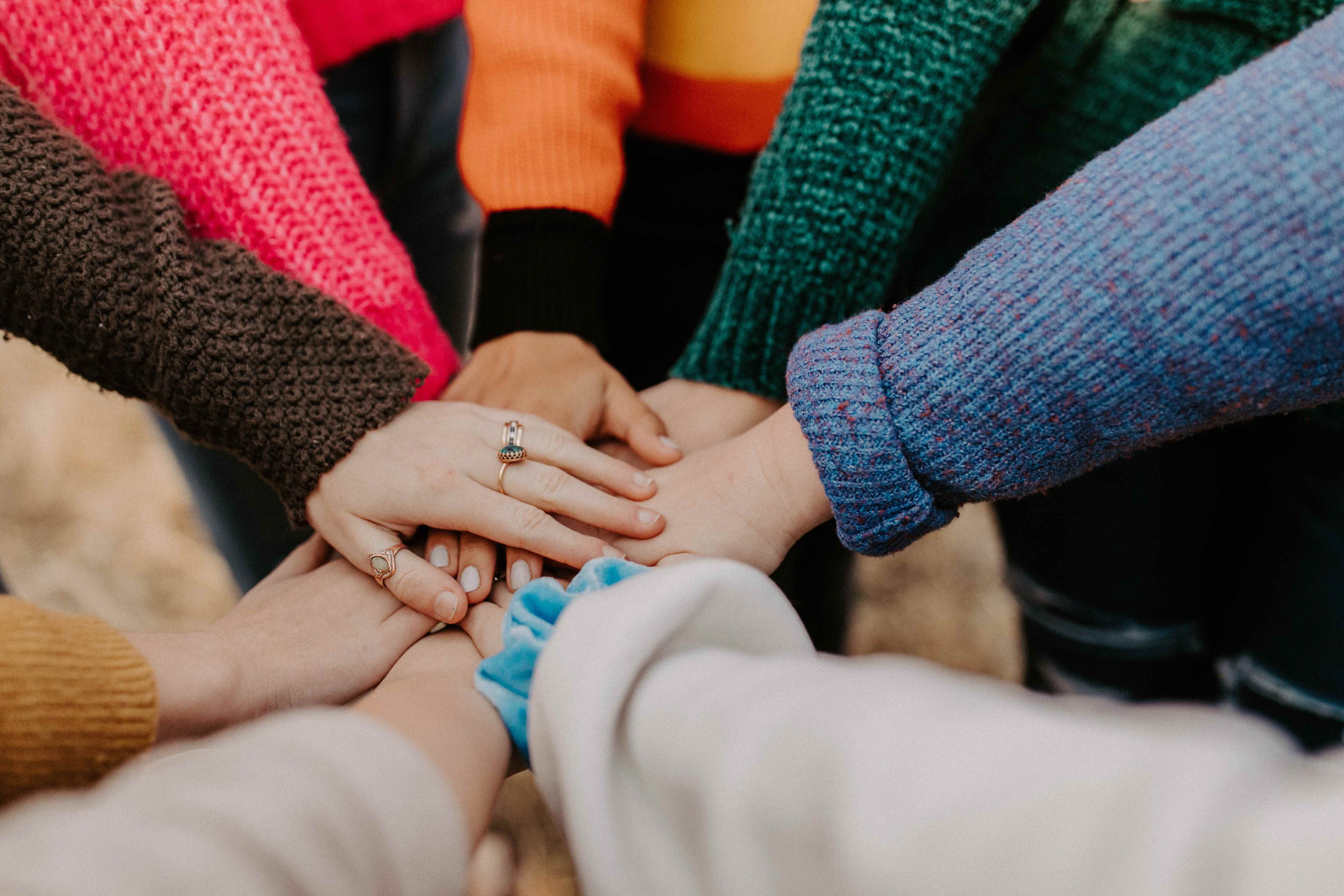Photo of a diverse group of eight people with hands stacked on top of one another in the middle of them expressing community and unity.
